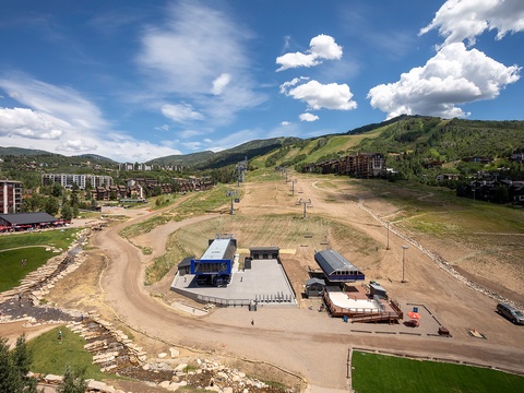 Aerial view of a mountain resort area featuring ski lifts and slopes, nestled among forested hills with nearby lodging and recreational facilities throughout the valley.