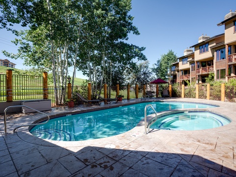 The property offers a sparkling outdoor pool and hot tub, surrounded by mature trees and rolling hillside views, perfect for unwinding after a day of mountain adventures.