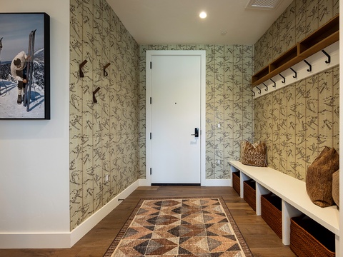 A charming mudroom welcomes you with rustic ski-themed wallpaper, built-in storage benches with woven baskets, and sturdy wooden hooks to stow your gear after a day of adventure.