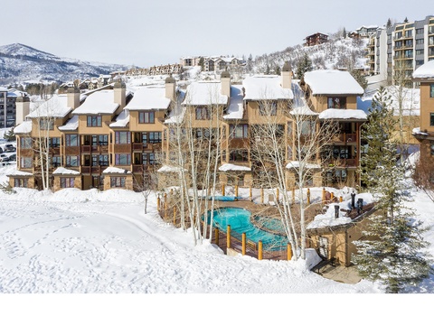 Aerial view of the property set in a scenic winter mountain resort, with ski-in access, outdoor pool, and surrounding alpine peaks blanketed in fresh snow.