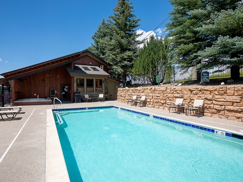 Sparkling outdoor pool framed by towering evergreens and mountain views, with cozy loungers ready for your alpine retreat.
