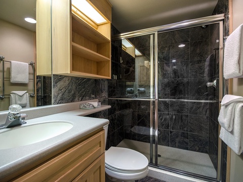 Step into your private bathroom with sleek dark marble tiles, a spacious walk-in shower, and fresh towels ready for your comfort.