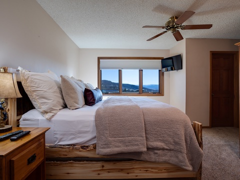 Drift off in a cozy bedroom framed by mountain vistas, where plush bedding and rustic wood furniture invite restful nights under a gentle ceiling fan.