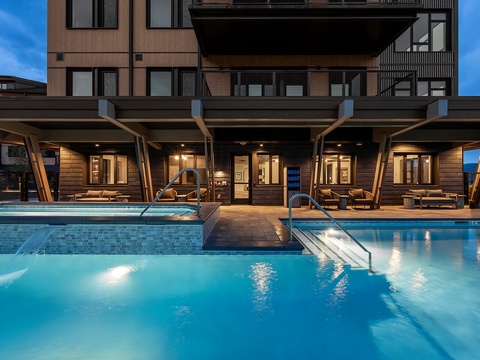 Modern mountain property featuring outdoor pools and covered lounge areas, captured during the tranquil twilight hour.