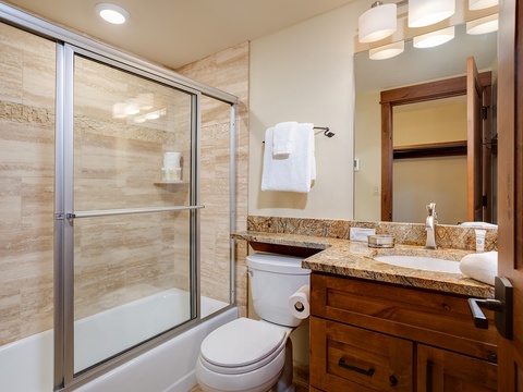 Step into your private bathroom featuring warm wood cabinetry, granite countertops, and a spacious shower-tub combo. Fresh towels await your arrival, ready for your comfort.