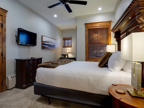 Your elegant retreat features a plush bed with luxurious linens, warm wood accents, a flat-screen TV, and charming bedside lighting—perfect for restful evenings after mountain adventures.