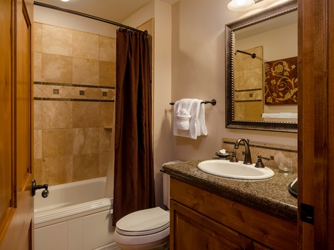 This tastefully designed bathroom features warm wood tones, elegant tile work, and a granite vanity for your comfort and relaxation.