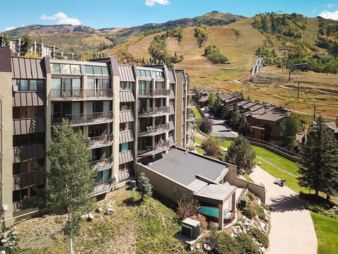 Aerial view of the vacation rental property nestled in a scenic mountain valley, surrounded by rolling ski slopes, evergreen forests, and neighboring alpine lodges.