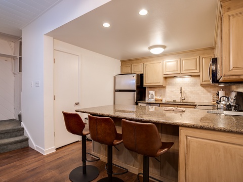 Gather around the breakfast bar in your fully equipped kitchen, where warm lighting and granite countertops create the perfect space for morning coffee or casual meals together.