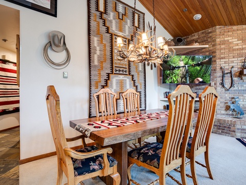 Gather around this handcrafted wooden dining table beneath a stunning antler chandelier. The rustic Southwestern décor, exposed brick wall, and warm wood ceiling create an inviting space where your group can share meals and make memories together.