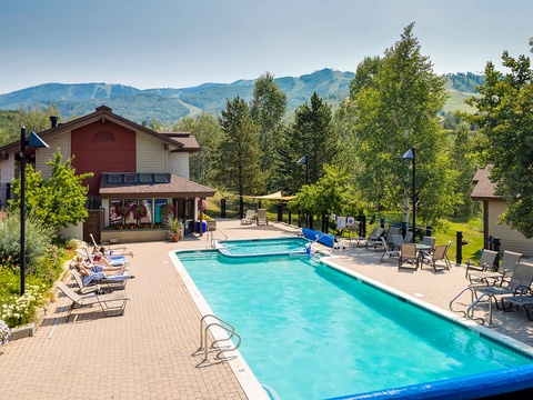 A sparkling outdoor pool framed by mountain views, with lounge chairs and shaded seating—perfect for relaxing under blue skies after a day of adventure.