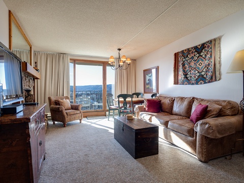 Sink into your spacious living room featuring a plush leather sofa, rich wood furnishings, and southwestern décor. Natural light floods through your private balcony doors, framing stunning mountain vistas that invite you to unwind in style.