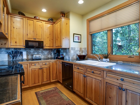Picture yourself cooking in this fully-equipped kitchen with warm wood cabinetry, granite counters, and natural light streaming through windows overlooking lush greenery.