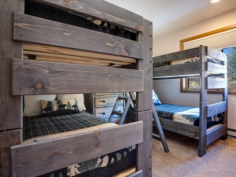 Rustic bunk beds with charming wildlife details offer cozy sleeping quarters, perfect for family gatherings. Natural light floods the room through wood-framed windows, creating a warm mountain retreat.