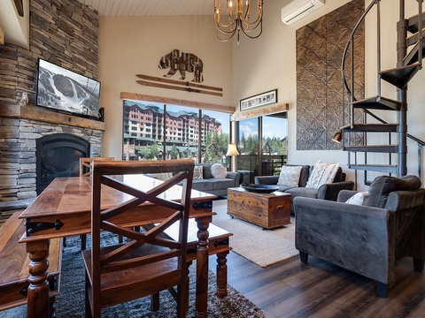 Your mountain retreat features soaring ceilings, rustic stone fireplace, and plush seating that invites you to unwind. Large windows frame stunning views, while the spiral staircase adds a charming loft touch.