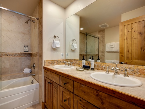 Refresh in your spacious guest bathroom featuring dual sinks, a relaxing tub, and walk-in shower with warm wood accents throughout.