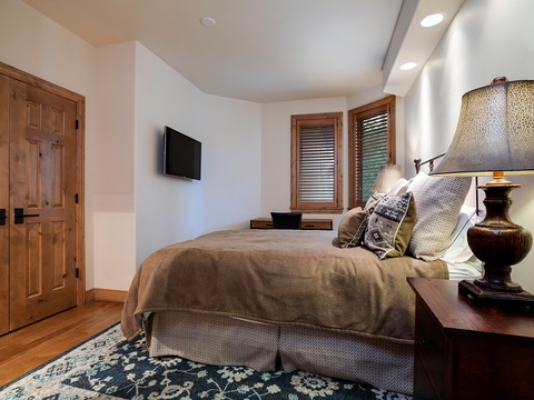 Drift off in your cozy retreat with warm wood tones, plush bedding, and serene natural light filtering through wooden shutters—your peaceful escape awaits.