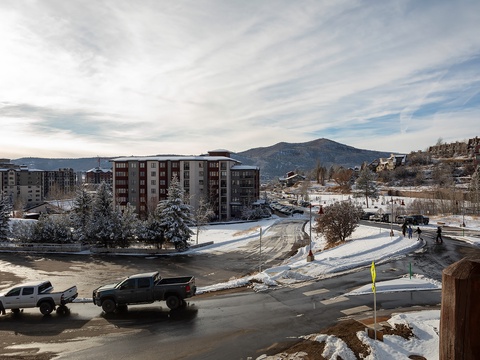 A winter mountain resort village nestled in snowy slopes, with multi-story buildings and scenic mountain peaks framing the surrounding area.