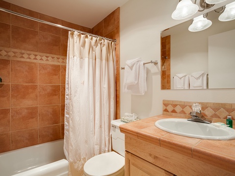 Your bathroom features warm terra-cotta tiles, a spacious tub with shower, and fresh towels ready for your arrival. Everything you need for a refreshing start to your day.