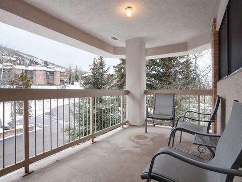 A covered balcony with comfortable seating overlooks snowy evergreens and mountain slopes, providing a peaceful spot to take in the alpine surroundings throughout the winter season.