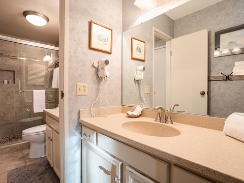 Your private bathroom features a spacious walk-in shower, fresh towels, and thoughtful touches like a hairdryer and framed artwork—designed to help you unwind in comfort.