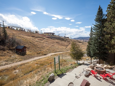 A patio offers views of a ski lift and mountainside, with red Adirondack chairs around a stone fire pit—perfect for après-ski relaxation.