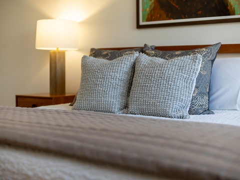 Sink into your plush bed surrounded by textured pillows and soft lighting—your cozy retreat awaits after a day of exploring.