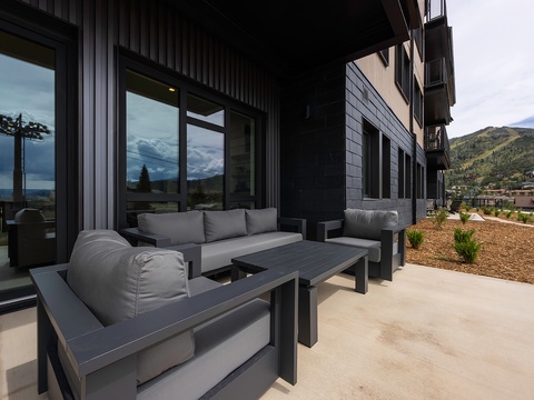 Modern mountain retreat featuring a covered patio with sleek outdoor furniture, perfect for relaxing while surrounded by stunning hillside views and fresh alpine air.