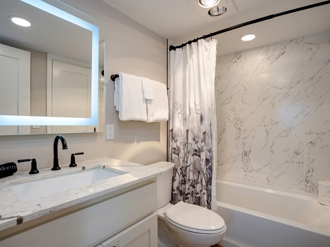 Step into your modern bathroom featuring elegant marble-look walls, a sleek tub-shower combo, and fresh linens ready for your arrival.