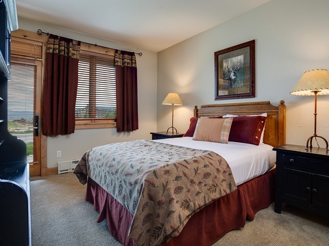 Your cozy retreat awaits with a plush bed dressed in rich burgundy tones, rustic wood accents, and soft lighting that creates the perfect ambiance for restful nights.