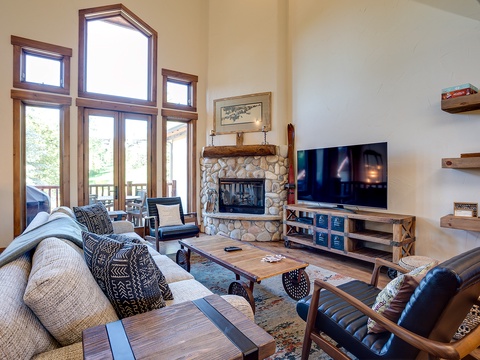 Curl up in this bright living room with soaring ceilings, a cozy stone fireplace, and expansive windows framing natural light. Perfect for gathering with loved ones or unwinding after your adventures.