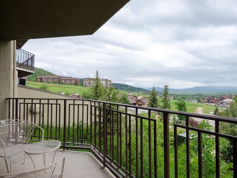 Private balcony offering expansive mountain and valley views across rolling green hills, nearby residential areas, and distant peaks under open skies.