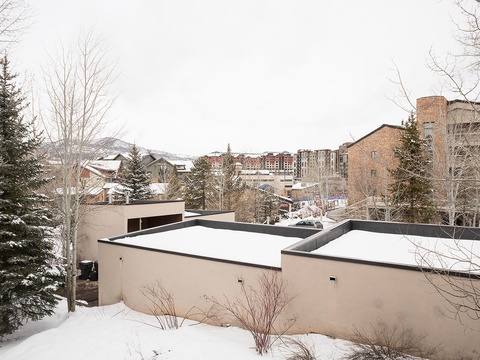 A tranquil winter scene showcasing the property nestled among snow-dusted evergreens with mountain resort buildings visible in the background, offering a peaceful alpine retreat setting.