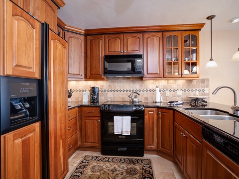 You'll love preparing meals in this well-appointed kitchen, featuring rich wood cabinetry, granite countertops, and modern appliances. The space includes a gas stove, refrigerator, microwave, dishwasher, and tiled backsplash—everything you need for a comfo