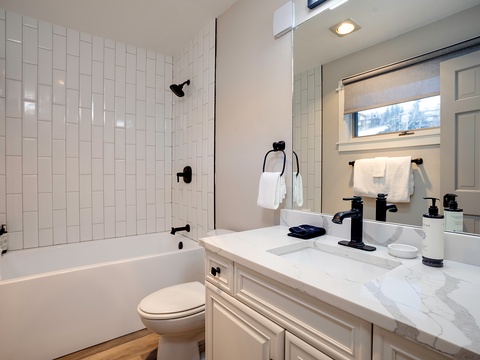 Step into your serene bathroom retreat with crisp white subway tiles, elegant marble countertops, and modern black fixtures. Fresh towels await your arrival, and the tub-shower combo invites you to unwind after a day of adventure.