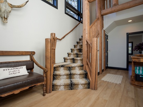 Step into a warm mountain retreat with rustic wood beams, a striking cowhide staircase, and charming touches like a leather bench and vintage skull decor—your perfect home base awaits.