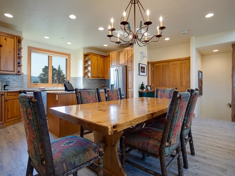 Gather around a handcrafted wood table under elegant chandelier light, with mountain views through the window. This warm, inviting dining space is perfect for shared meals and lasting memories.