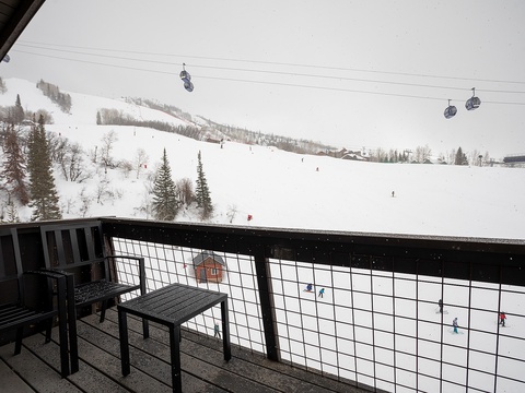 Ski resort featuring snow-covered slopes, ski lifts, and nearby evergreen forest. Private balcony with outdoor seating and scenic slope views.