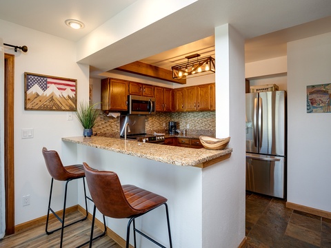Pull up a seat at your granite breakfast bar and enjoy morning coffee in this well-appointed kitchen with warm wood cabinetry, modern appliances, and thoughtful lighting overhead.