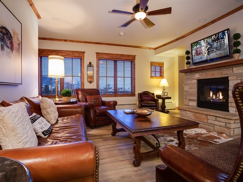 Relax in your spacious living room with warm wood accents, plush leather seating, a crackling fireplace, and a large TV for cozy evenings after your mountain adventures.