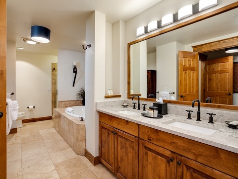 Your spacious bathroom features dual vanities with elegant marble countertops, warm wood cabinetry, and a relaxing soaking tub where you can unwind after a day of adventure.