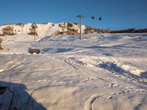 A ski resort base area showcases snowy slopes, ski lifts, and surrounding buildings under clear winter skies, offering access to mountain recreation.