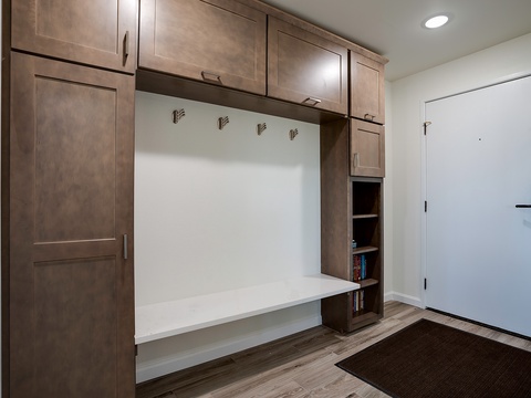 This smart entryway features custom built-in storage with warm wood cabinetry, a convenient bench for removing shoes, and hooks for coats—keeping your arrival effortlessly organized.