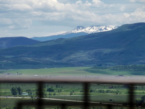 A stunning snow-capped mountain rises beyond rolling forested hills and green valleys, capturing the dramatic natural landscape surrounding the property area.