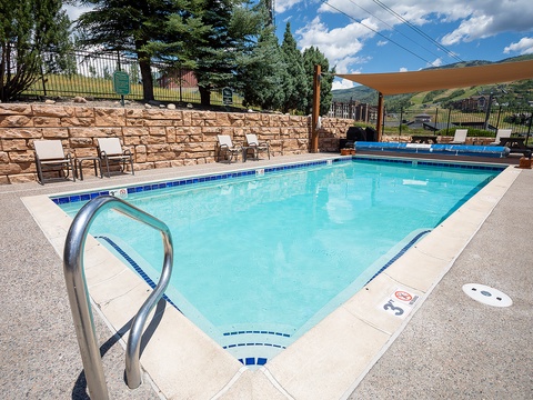 Sparkling outdoor pool framed by stone walls and mountain views, with shaded loungers ready for your sunny afternoon escape.