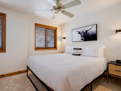 Sink into crisp white linens beneath a gentle ceiling fan, where warm wood accents and modern art create your peaceful mountain retreat.