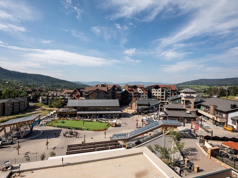 Aerial view of a mountain resort village surrounded by forested hillsides, showcasing the property's scenic alpine setting and convenient access to recreational amenities.