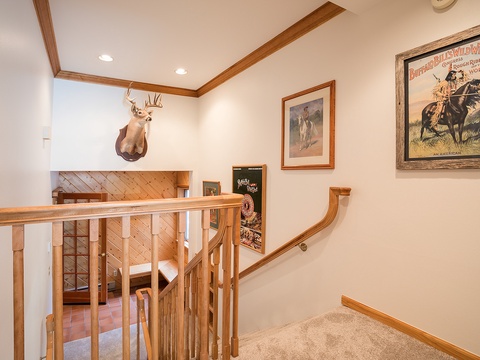 A stairwell leading to the lower level, adorned with Western-themed artwork and a mounted deer head, captures the rustic charm of your mountain retreat.
