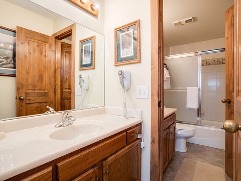 Freshen up in this bright, welcoming bathroom featuring a spacious vanity, large mirror, and full bathtub-shower combo—your private retreat after a day of mountain adventures.