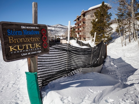 Ski access sign marks trails to Storm Meadows, Bronzetree, and Kutuk condominiums, with snowy slopes and a multi-story alpine building in the mountain setting.